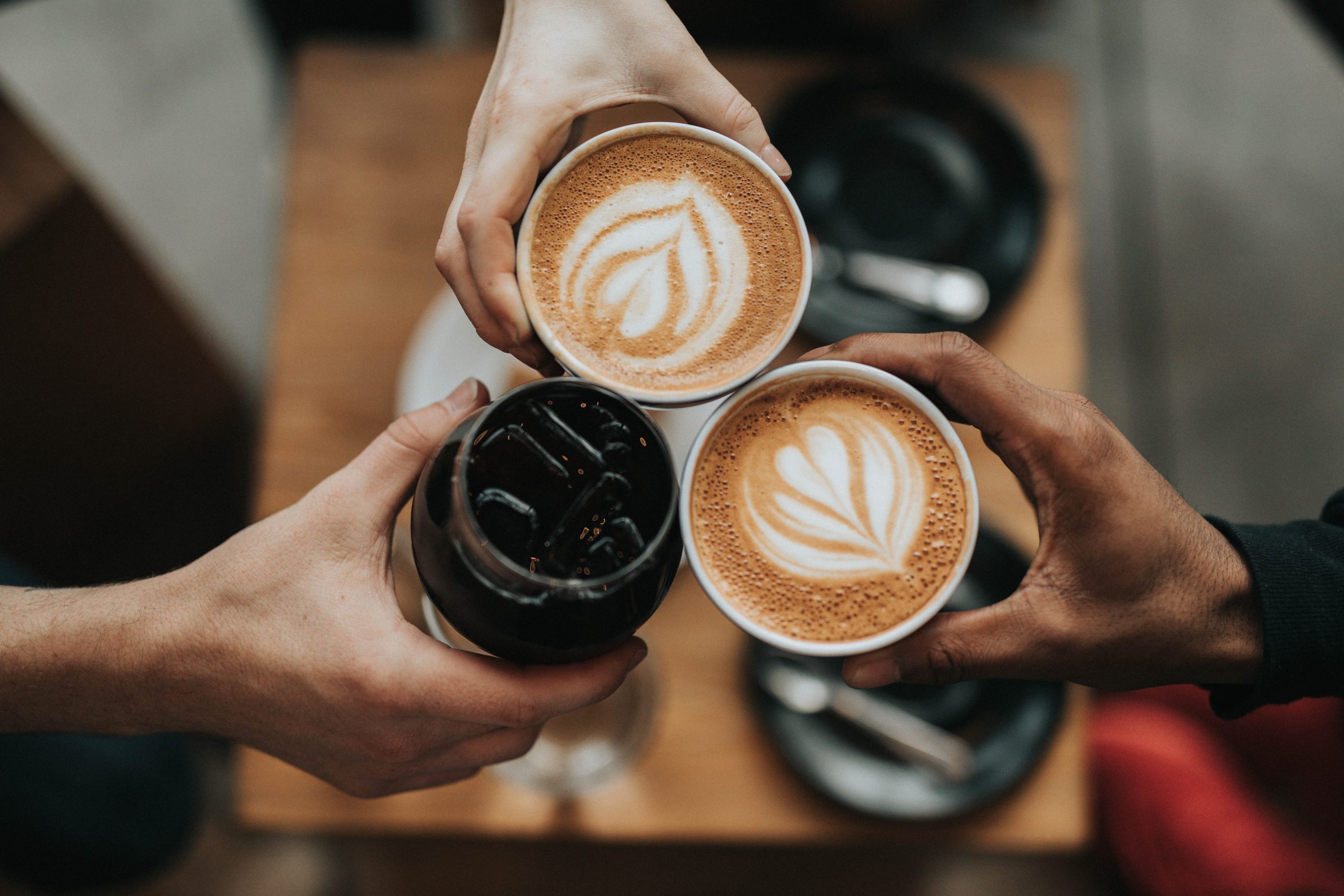 Three outstretched hands holding coffee cups